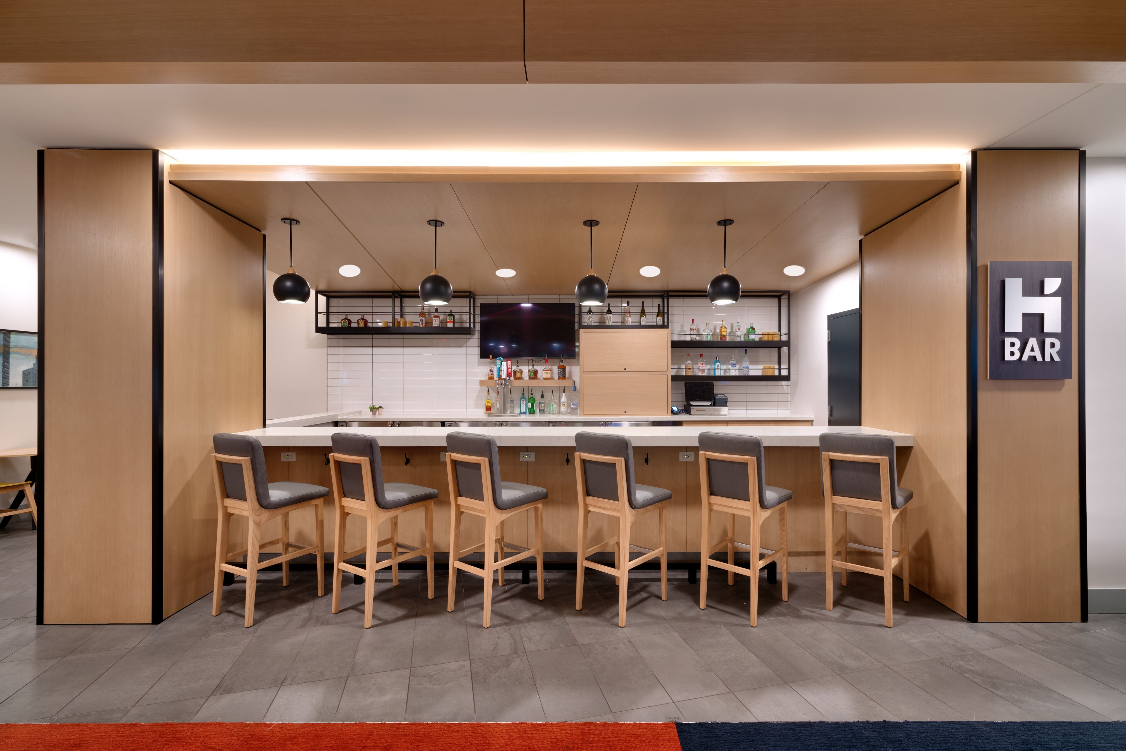 A bar area with wooden bar stools, a counter, and shelves with bottles.