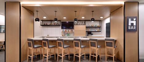 A bar area with wooden bar stools, a counter, and shelves with bottles.