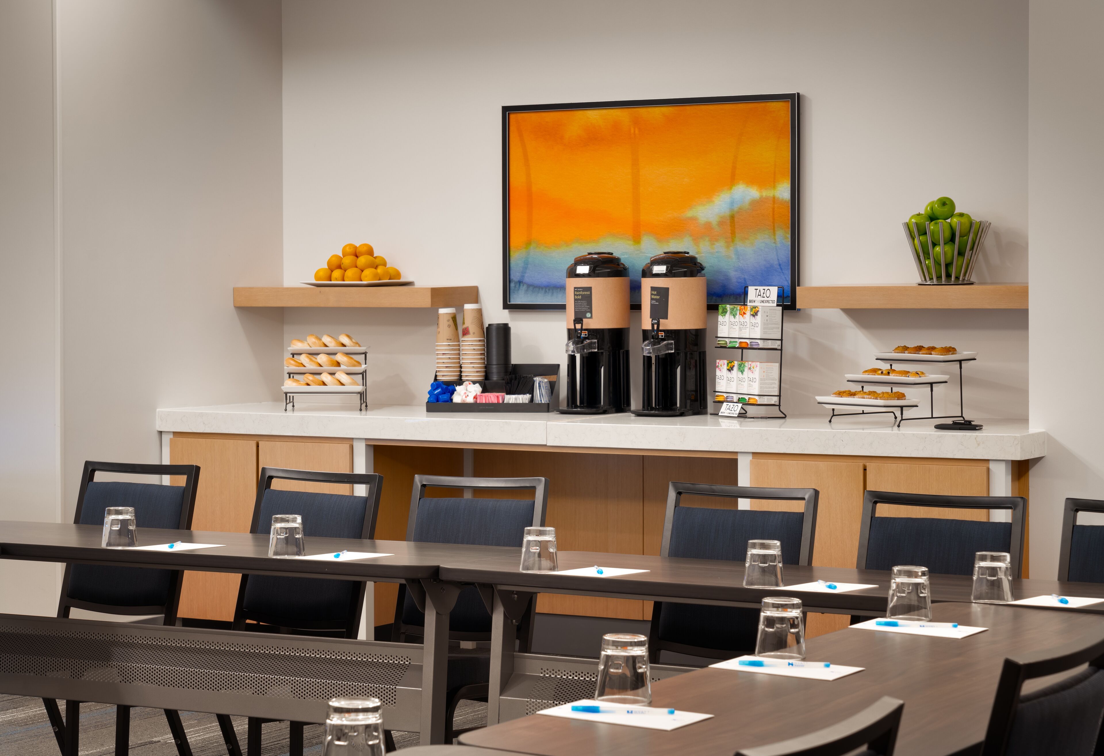 Una sala de conferències amb una taula llarga, cadires, cafetera i una presentació de fruita.