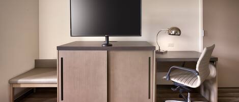 A hotel room with a bed, a desk with a computer monitor, a lamp, and a chair.