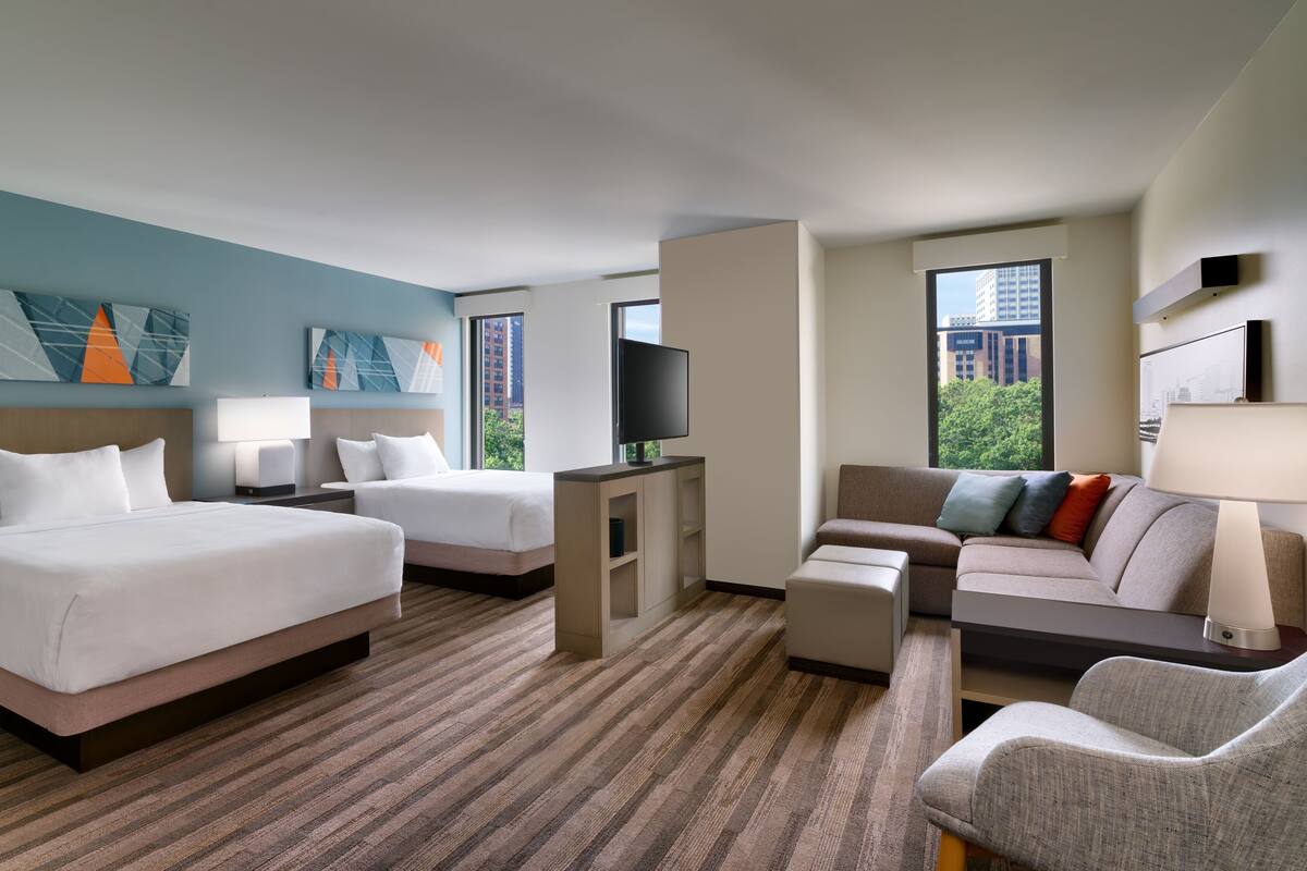 A hotel room with two beds, a sofa, a TV, and artwork on the walls.