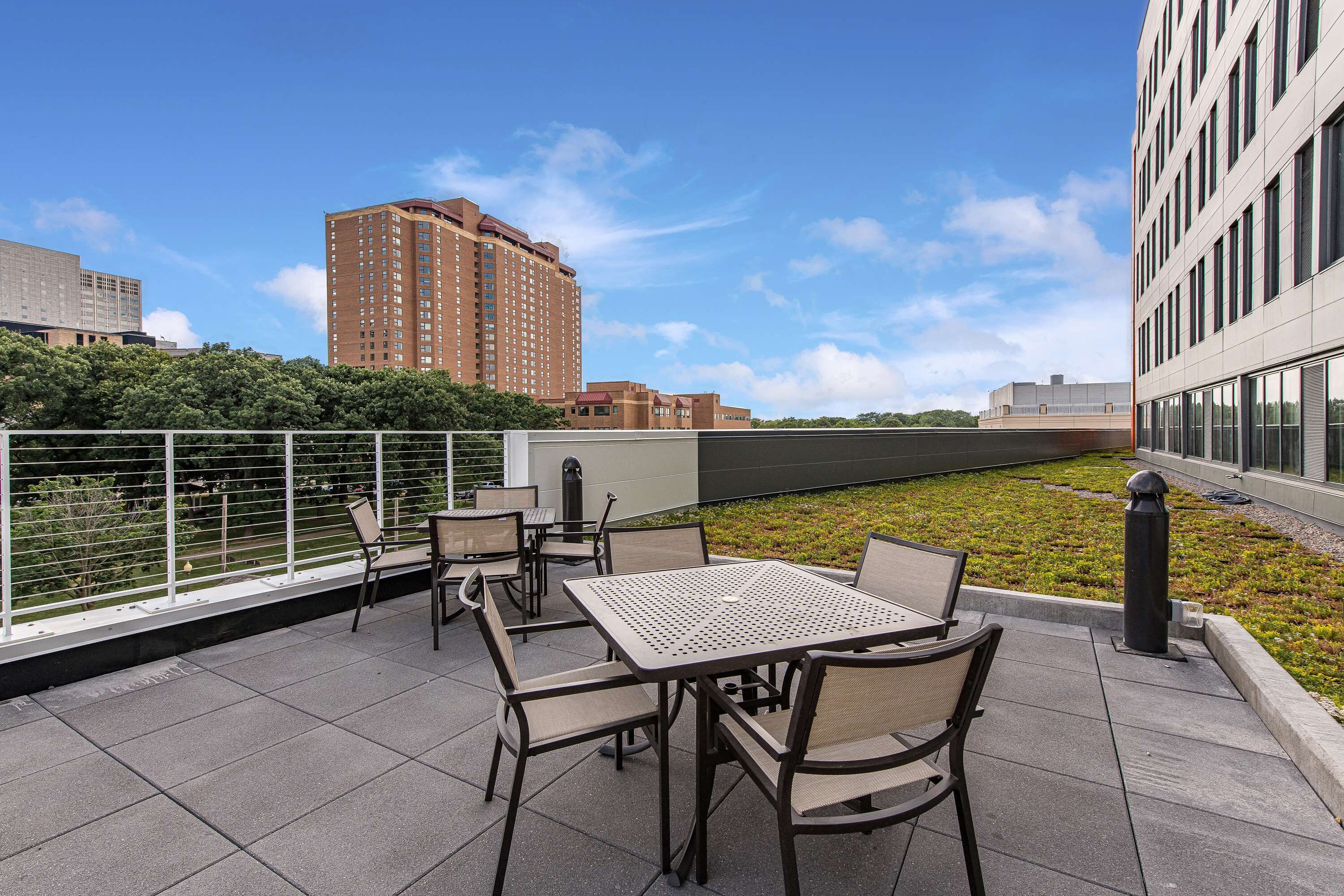 A rooftop terrace with outdoor seating, a view of a cityscape, and a landscaped area.