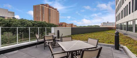 A rooftop terrace with outdoor seating, a view of a cityscape, and a landscaped area.