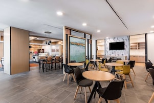 Un comedor moderno con mesas y sillas redondas, un cuadro grande en la pared y un televisor de pantalla plana montado sobre un muro con diseño geométrico.