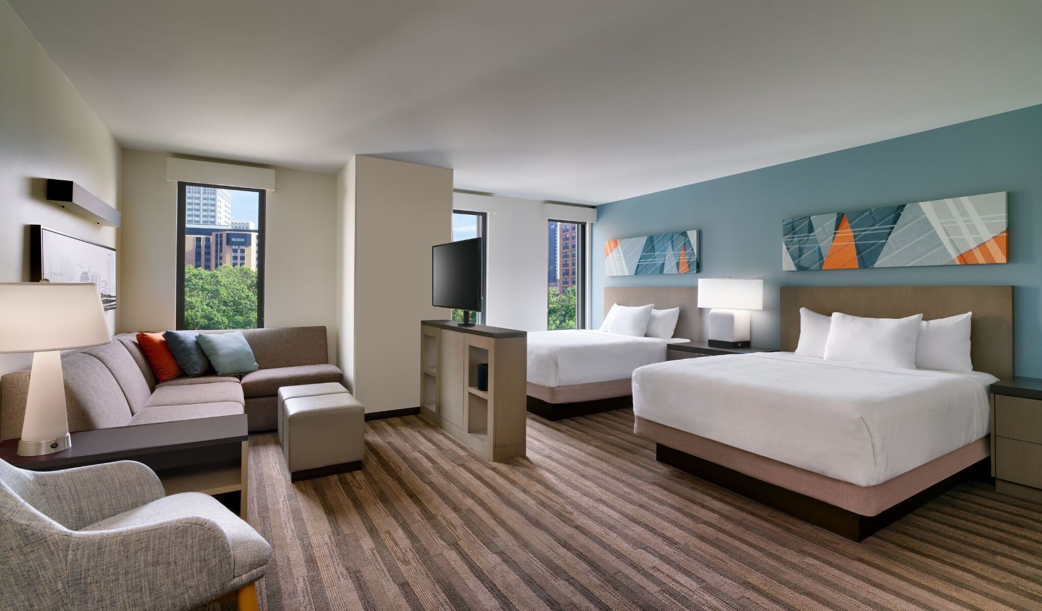 A hotel room with a sofa, two beds, a TV, and artwork on the walls.