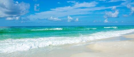 A beach with clear turquoise water and white sand under a bright blue sky.