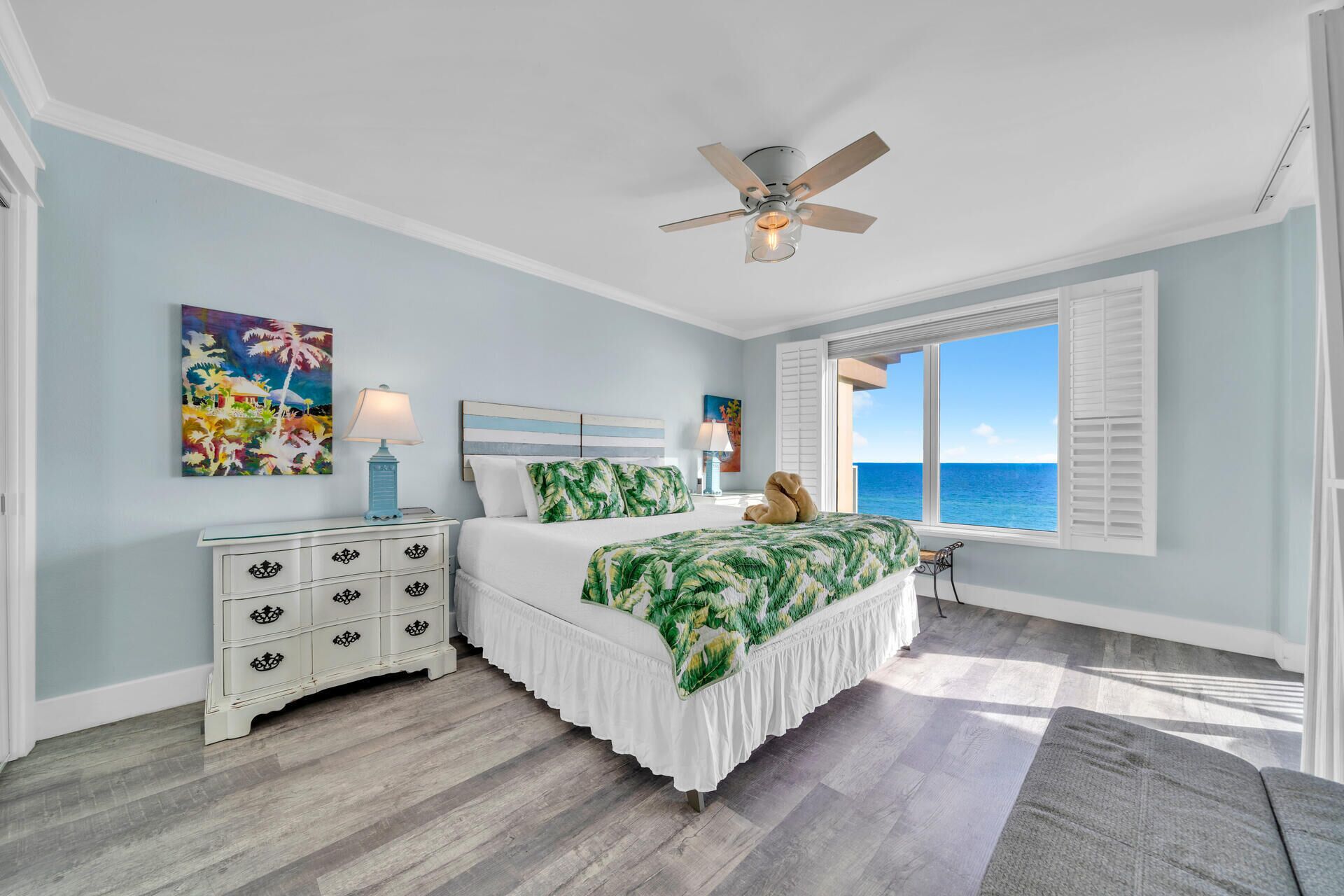 A bedroom with a bed, a nightstand, a ceiling fan, and a window with a view of the ocean.