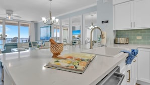 Une cuisine moderne dotée d’un grand îlot central, de meubles blancs et offrant une vue sur l’extérieur.