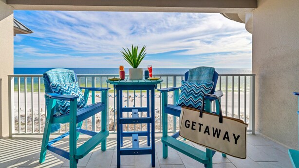Un balcon avec des chaises turquoise, une petite table et une pancarte indiquant « ÉVADEZ-VOUS ».