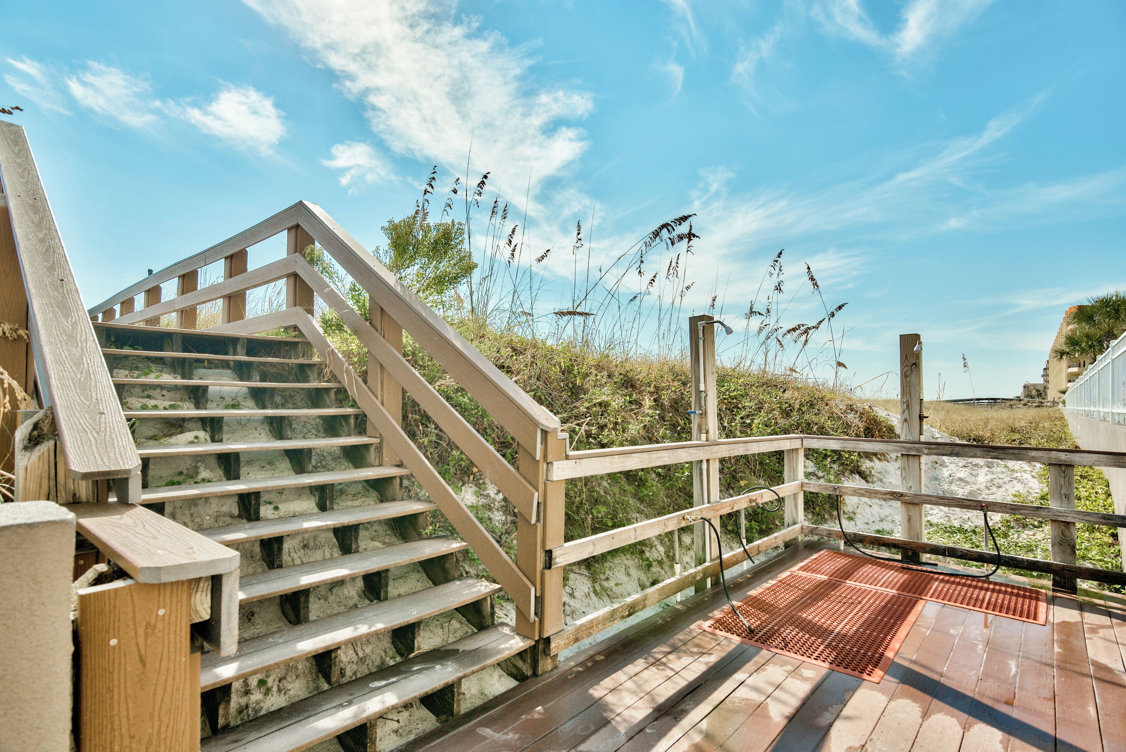 Una escalera de madera que lleva a una terraza con rejilla metálica, rodeada de vegetación natural.