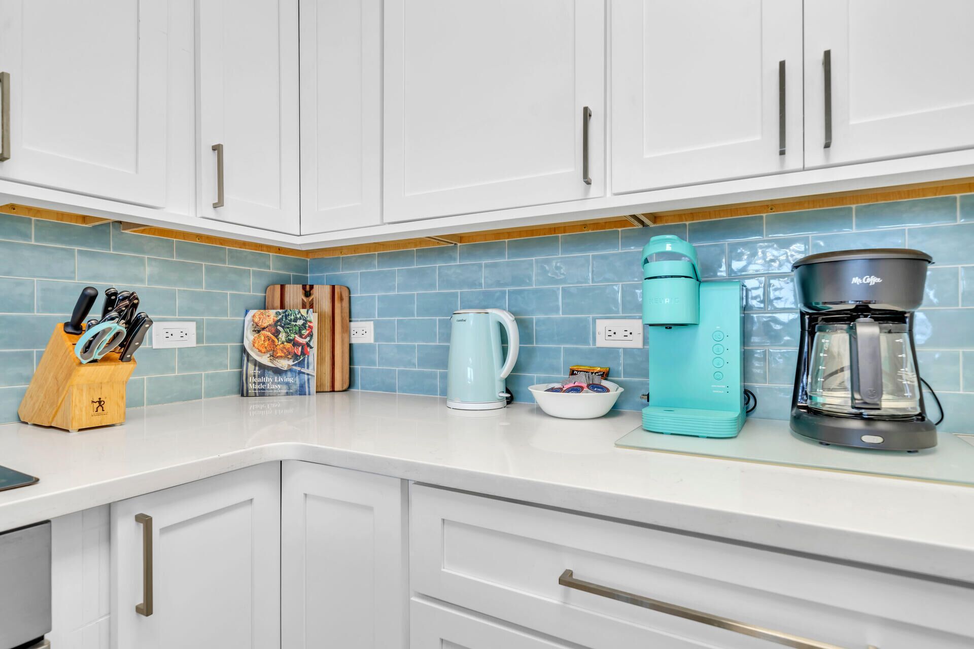Cucina con pensili bianchi, zoccolo di piastrelle blu, una moka e un bollitore.