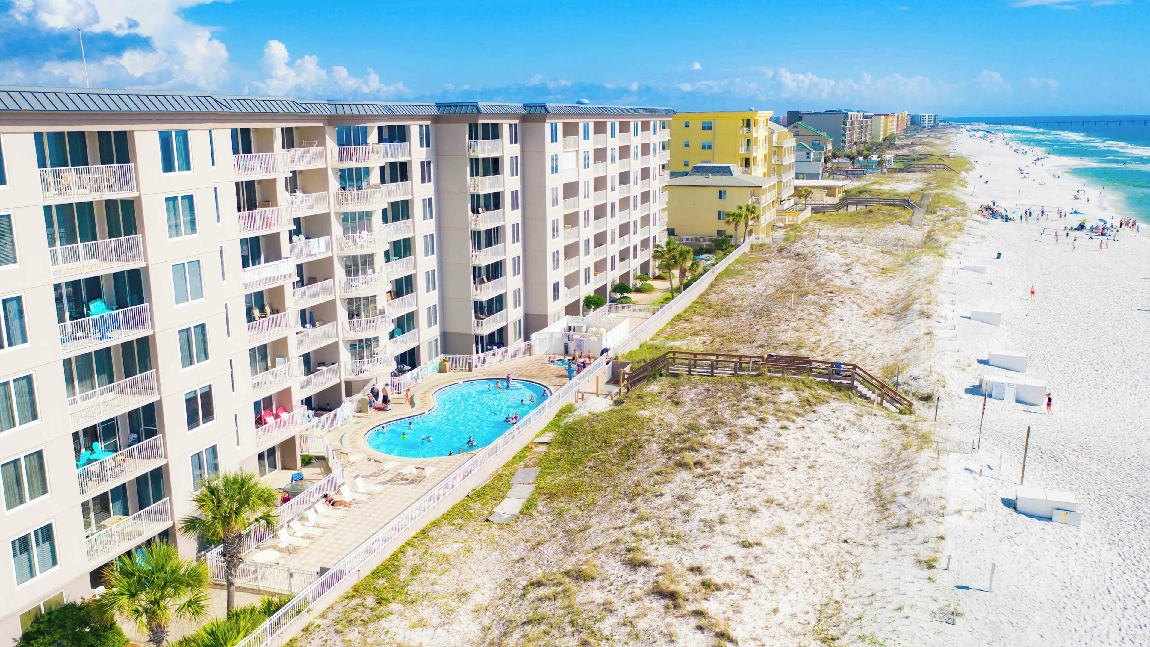 A hotel with multiple balconies, a swimming pool, and a beach view.