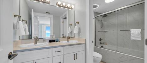 A modern bathroom with two sinks, a large mirror with lights, a shower with glass doors, and a toilet.