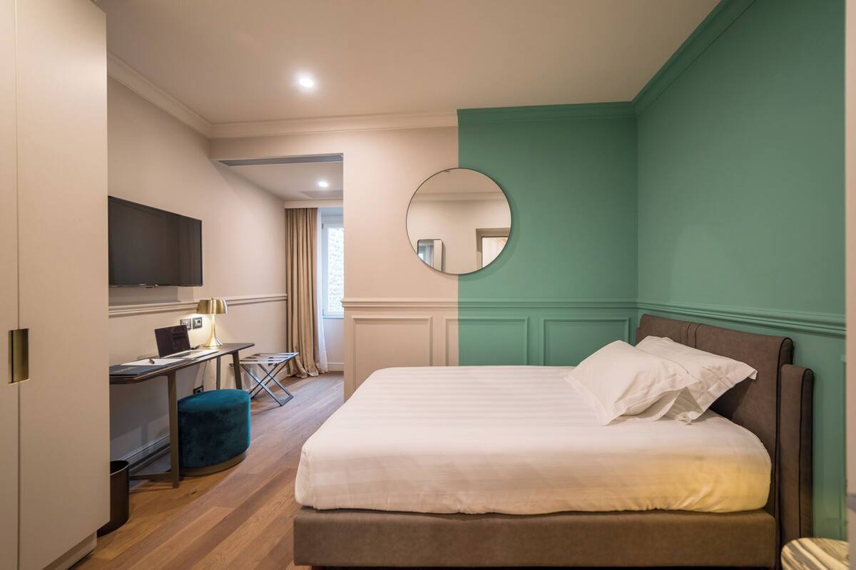Un dormitorio con cama, escritorio, silla, televisor y espejo.