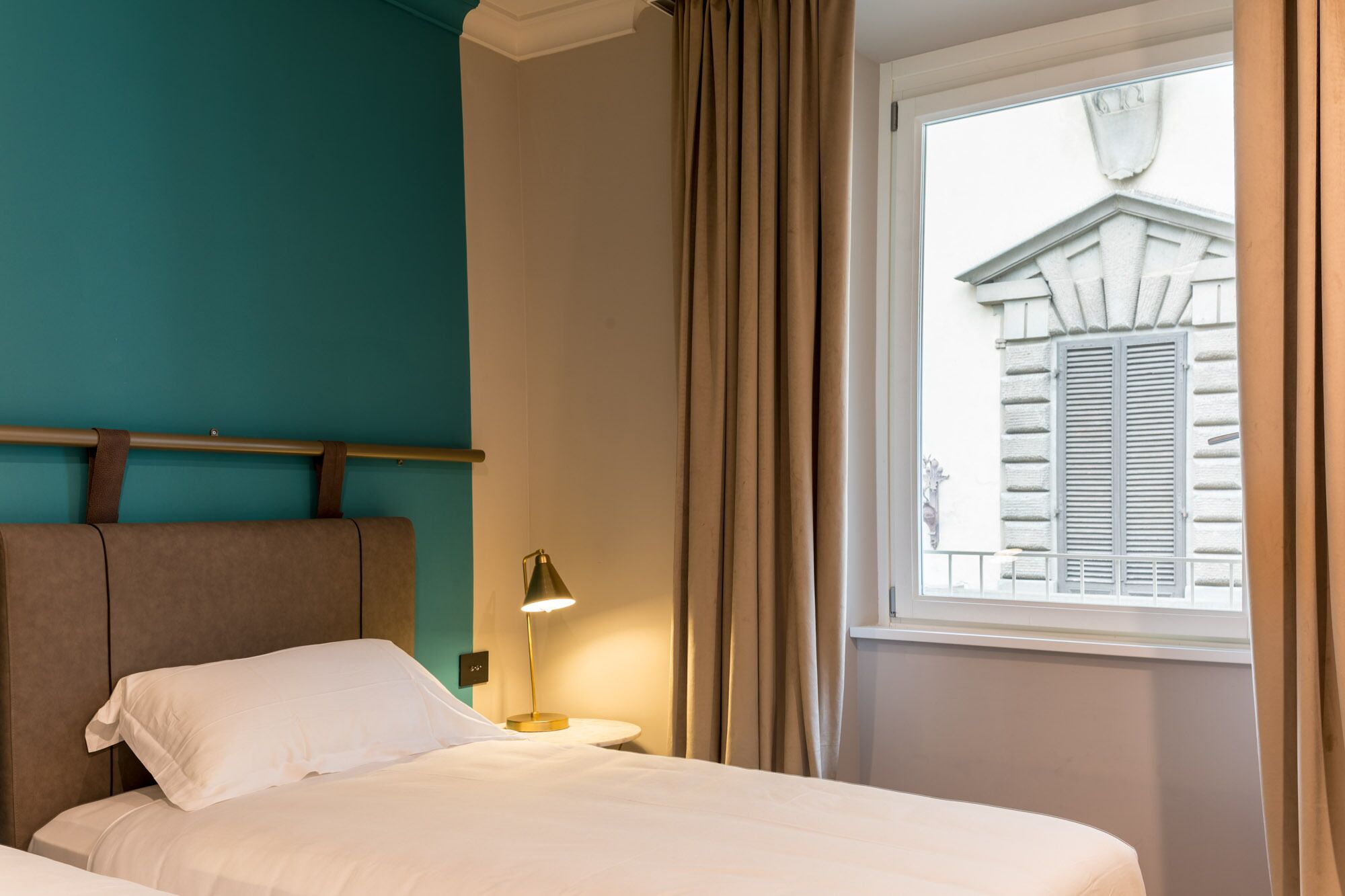 Una habitación de hotel con una cama, una mesita de noche, una lámpara y una ventana con cortinas.