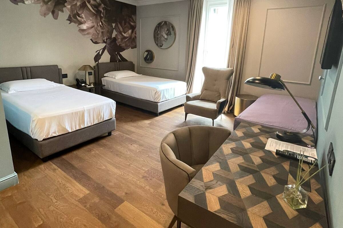 Habitación de hotel con dos camas, un escritorio, una silla, una lámpara y una decoración floral grande en la pared.