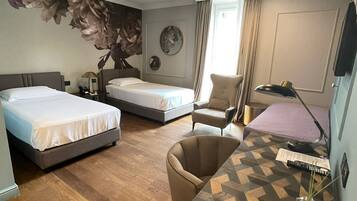 Une chambre d’hôtel avec deux lits, un bureau, une chaise, une lampe et une grande décoration murale à motifs floraux.