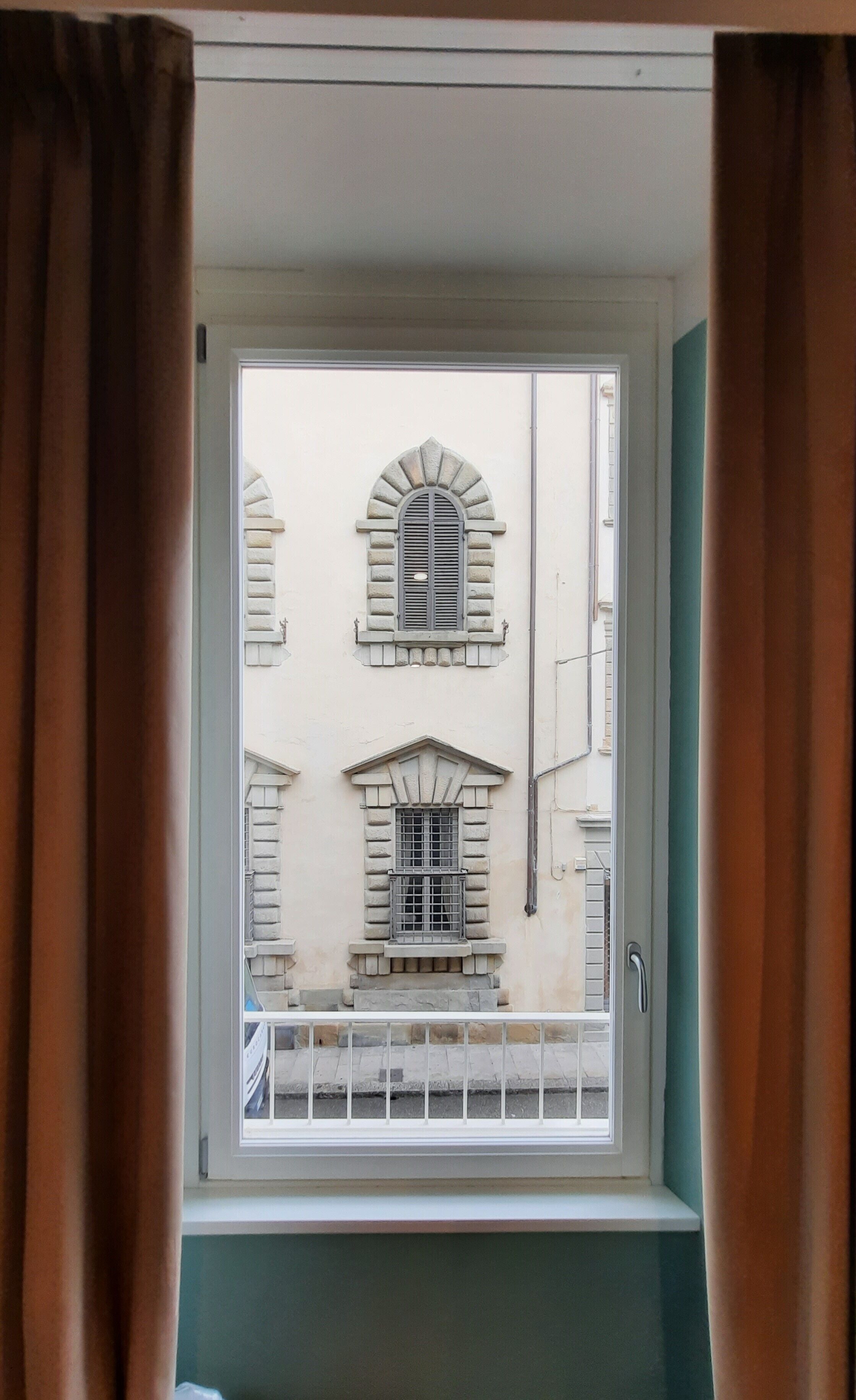 Una ventana con vista a un edificio que tiene dos ventanas arqueadas y una barandilla de balcón.