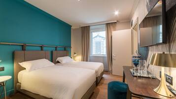 Een hotelkamer met twee bedden, een bureau met lamp, een televisie en een raam met gordijnen.