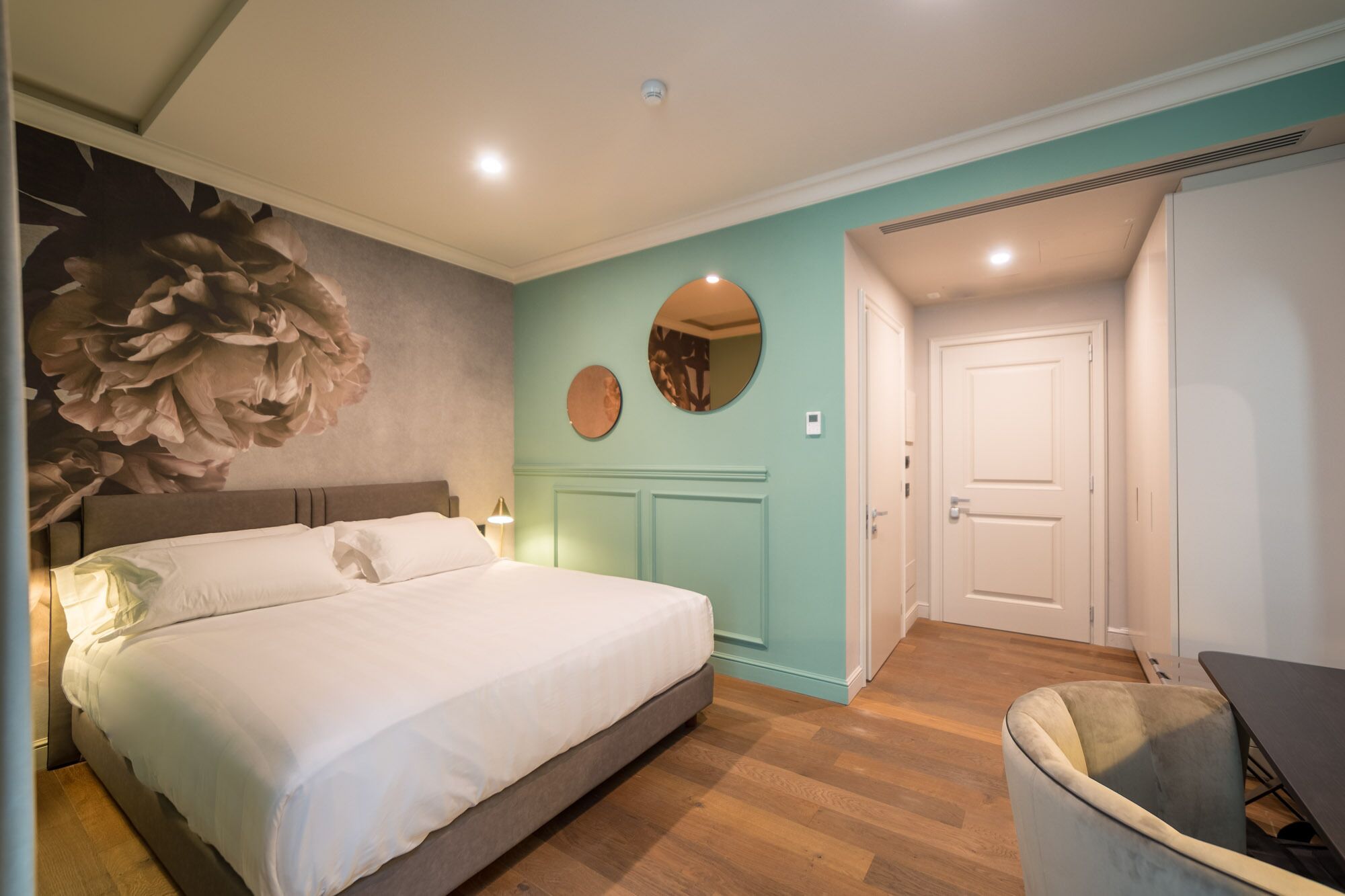Une chambre à coucher avec un grand lit, un miroir rond et une porte donnant sur une autre pièce.