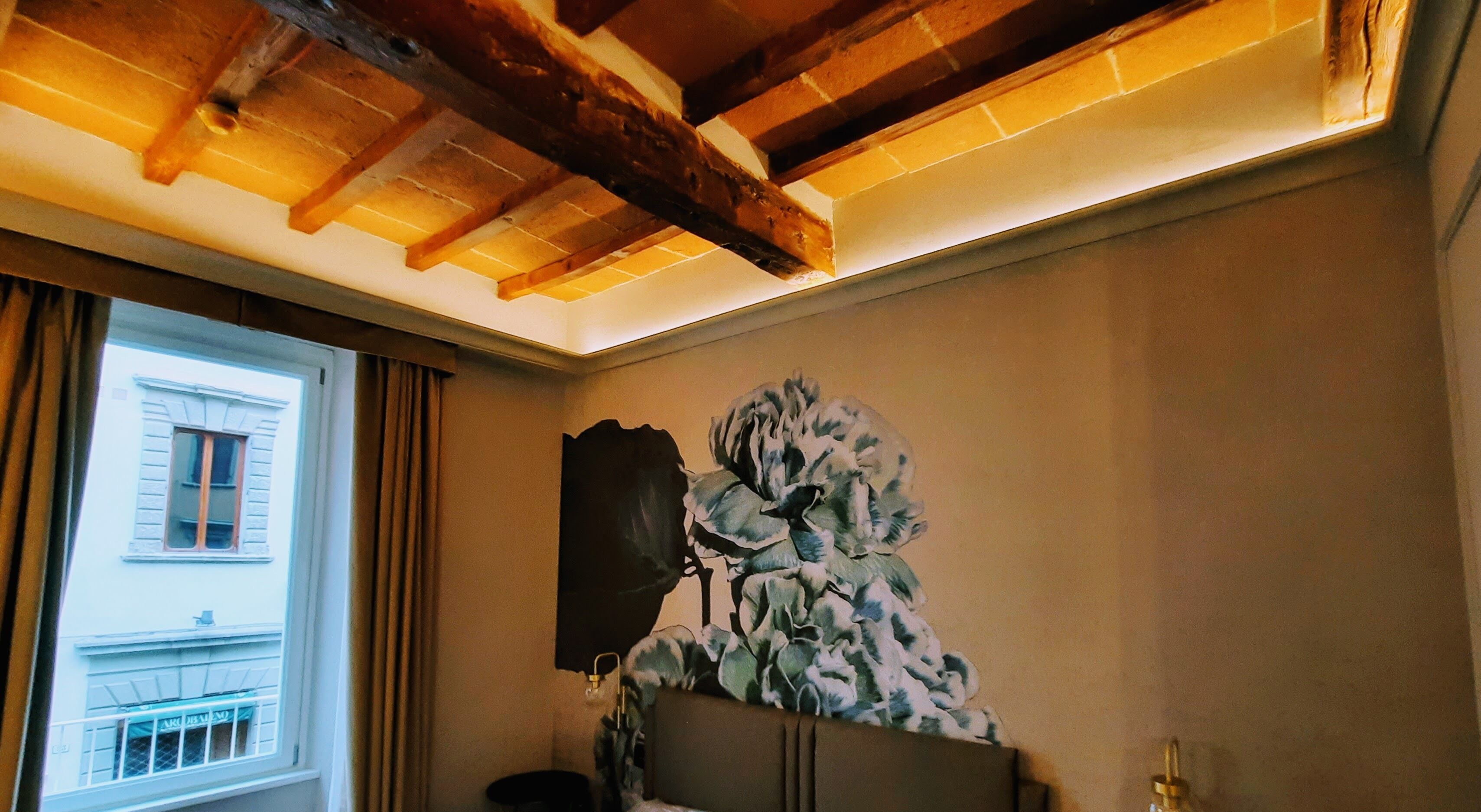 Una habitación con techo de madera, un ventanal con cortinas y una obra de arte colgada en la pared.