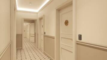 Un corridoio d'albergo con pavimento a motivi, pareti bianche e porte con numeri civici.