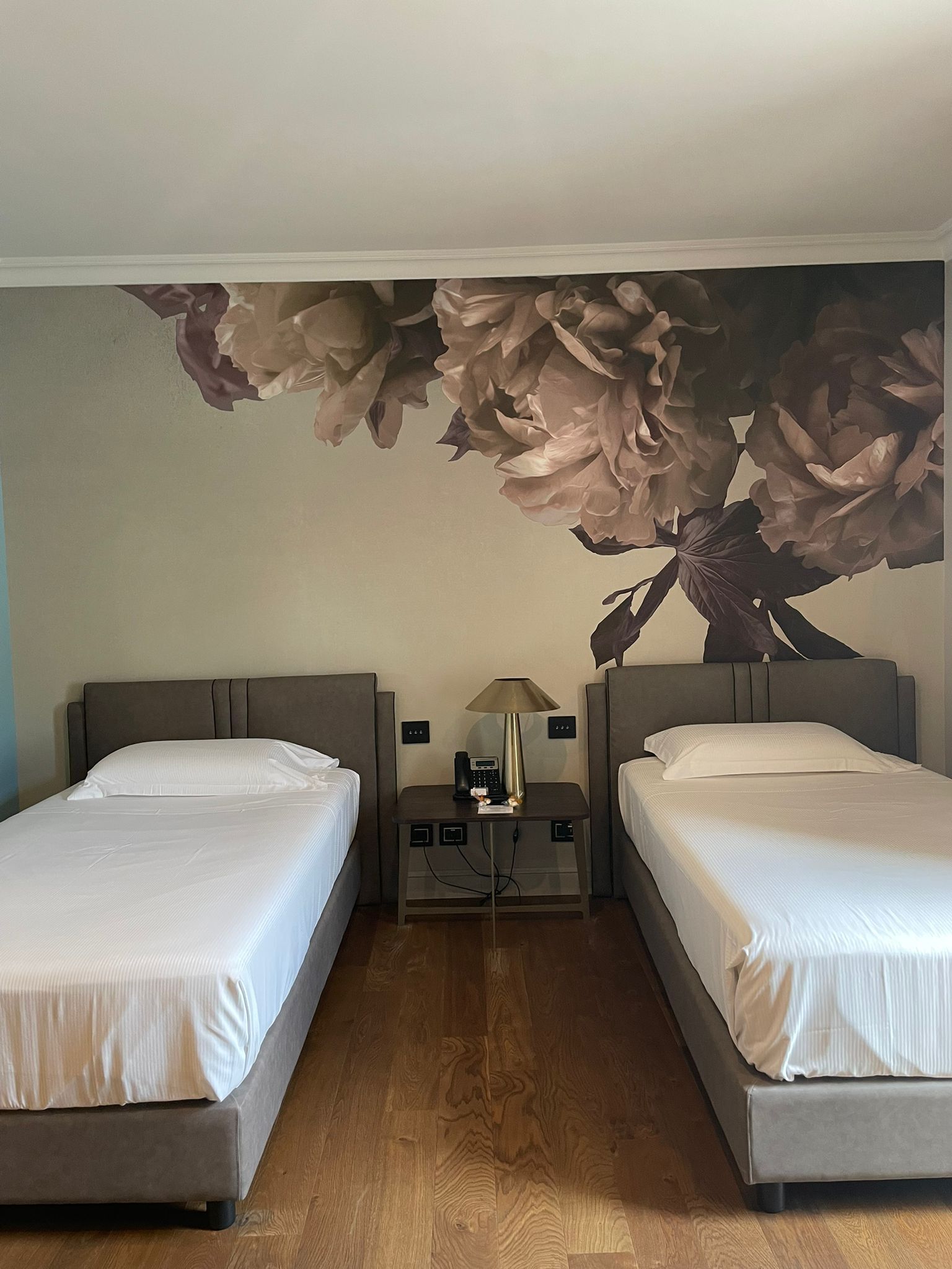 A hotel room with two beds, a nightstand with a lamp, and a large floral mural on the wall.