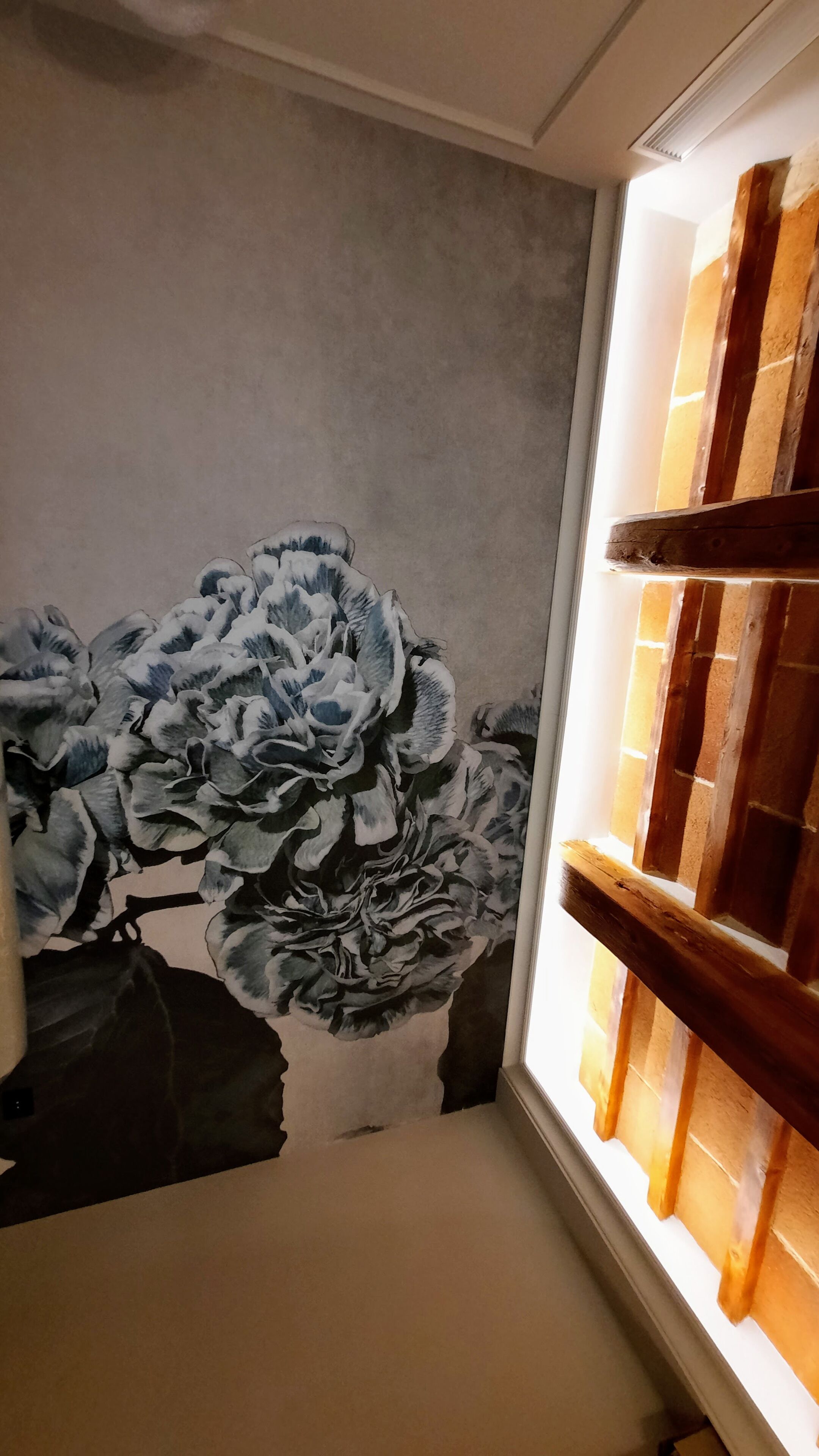 Quarto com um grande mural floral na parede, uma janela com persianas de madeira e teto branco.