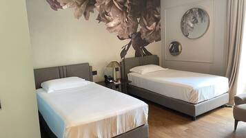 Habitación de hotel con dos camas, un mural grande con motivos florales en la pared, un espejo redondo y suelo de madera.