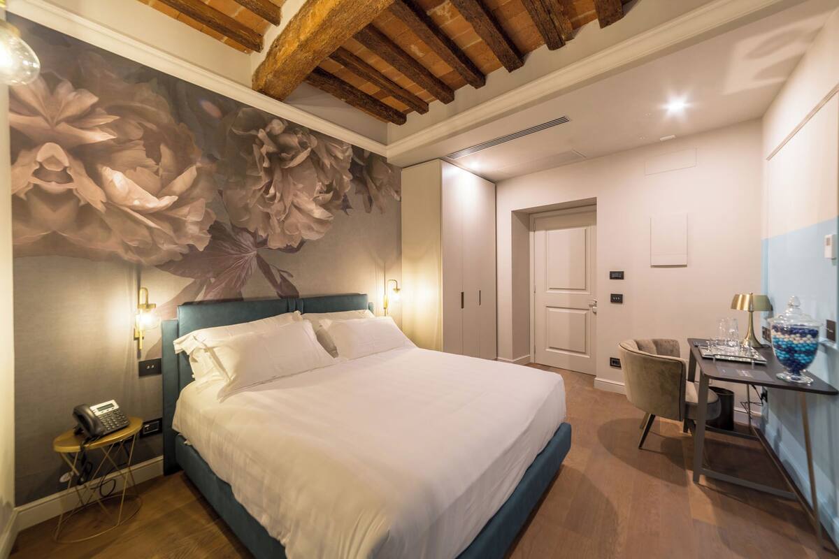 Habitación de hotel con una cama grande, un escritorio con silla, un teléfono y un papel tapiz floral en la pared.