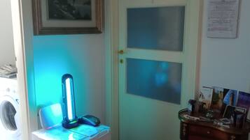 Une pièce comprenant un lave-linge, un bureau avec une lampe, une porte avec des panneaux en verre dépoli et un mur orné d’un tableau et de quelques documents.