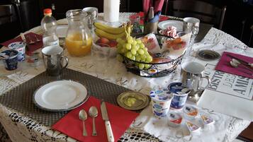 Une table de petit-déjeuner dressée avec des assiettes, des couverts, un panier de fruits et divers aliments pour le petit-déjeuner.