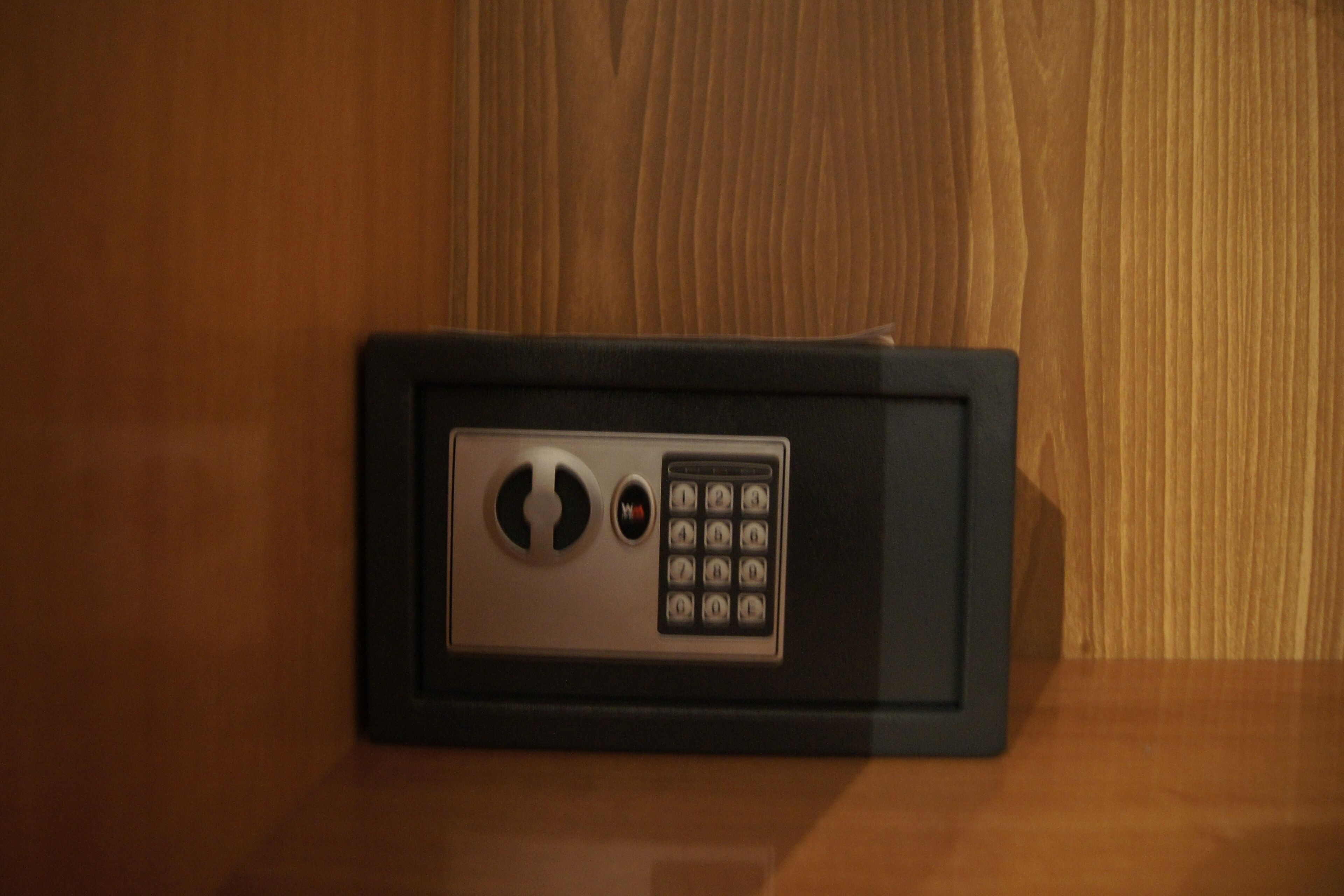 A safe with a keypad and a keyhole, placed on a wooden surface.