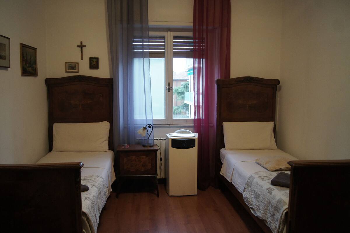 Un dormitorio con dos camas de madera, una mesita de noche, un calentador y una ventana con cortinas.