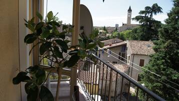 Un balcon orné d’un pot de fleurs, une vue sur une ville avec un beffroi et un toit recouvert de tuiles.