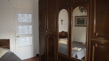Une chambre avec une grande armoire en bois, un lit avec un oreiller blanc et une croix accrochée au mur.