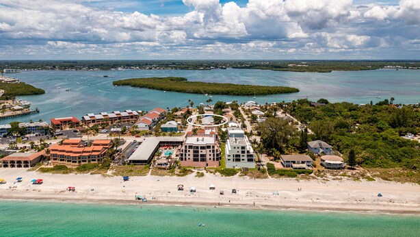 Vista aérea de un complejo turístico costero con propiedades frente a la playa, un puerto deportivo y aguas turquesas cristalinas.