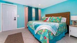 Un dormitorio con cama, mesita de noche, lámpara, puerta y cortinas.