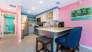 Una cocina con pared rosa, un cuadro de una playa y un refrigerador.
