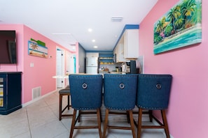 A kitchen with white cabinets, a refrigerator, and a microwave. There are three blue chairs with metal rings.