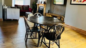 A dining area with a round table and four chairs, a red sofa, a fireplace, and a television mounted on the wall. - Bodhi Tree Cottage - Grove Road Cottages (Stratford-upon-Avon)