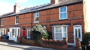 A row of terraced houses with brick facades, white-framed windows, and a red door. - Bodhi Tree Cottage - Grove Road Cottages (Stratford-upon-Avon)