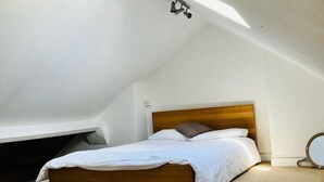 A bedroom with a sloped ceiling, a wooden bed frame, and a small round mirror on the wall. - Bodhi Tree Cottage - Grove Road Cottages (Stratford-upon-Avon)