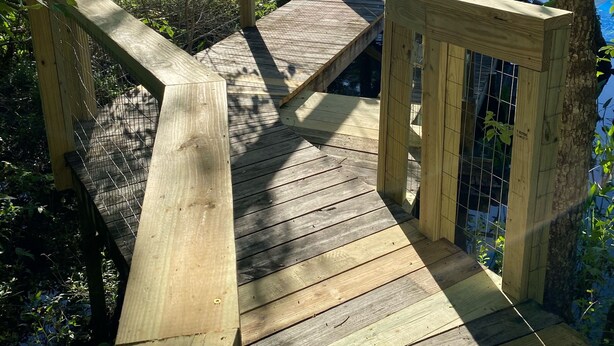 A wooden bridge with a railing, leading to a wooden platform with a bench.