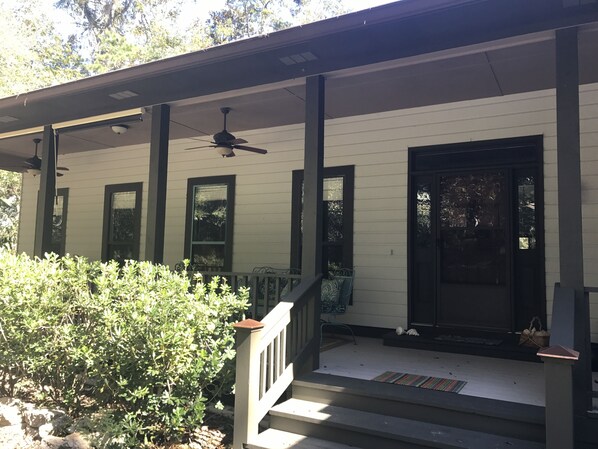 A covered porch with a black door, white siding, and a ceiling fan.