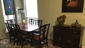 A dining area with a wooden table and chairs, a floral rug, a cabinet with decorative items, and a painting on the wall.