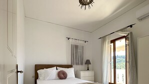 A bedroom with a bed, a nightstand, a lamp, and a view of the outdoors through a door. - Penthouse sea view suite (Parga)