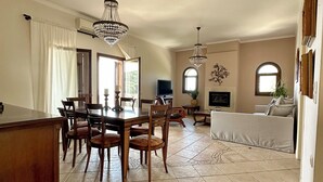 A spacious living area with a dining table and chairs, a sofa, and a TV. - Penthouse sea view suite (Parga)