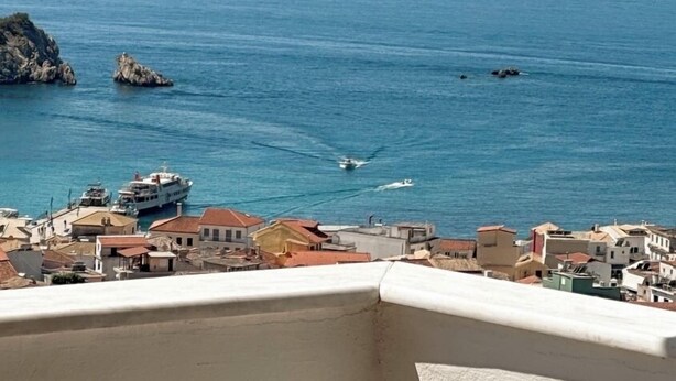 A coastal town with buildings along the waterfront, boats on the sea, and rocky outcrops. - Penthouse sea view suite (Parga)