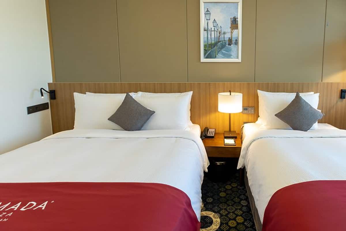 A hotel room with two beds, a nightstand with a lamp, a painting on the wall, and a chair.